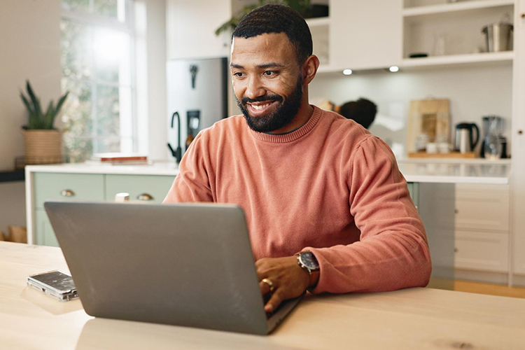 Image of a man looking enthusiastically at his laptop computer inside a brightly lit and cheerful home.
