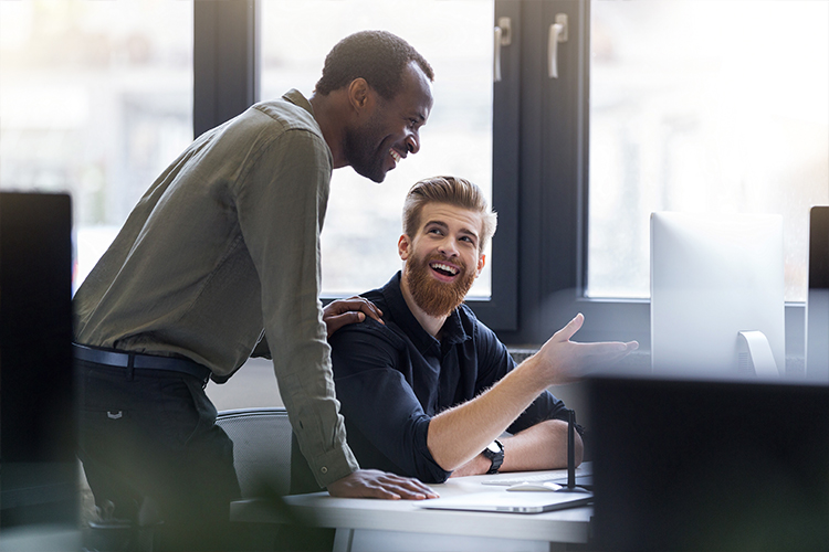 Two men having a conversation in an office setting with happy expressions on their faces
